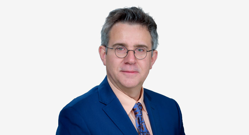 Bartosz Szczesney, PhD, appears in a professional headshot, wearing a blue jacket, blue patterned tie and pastel peach shirt.