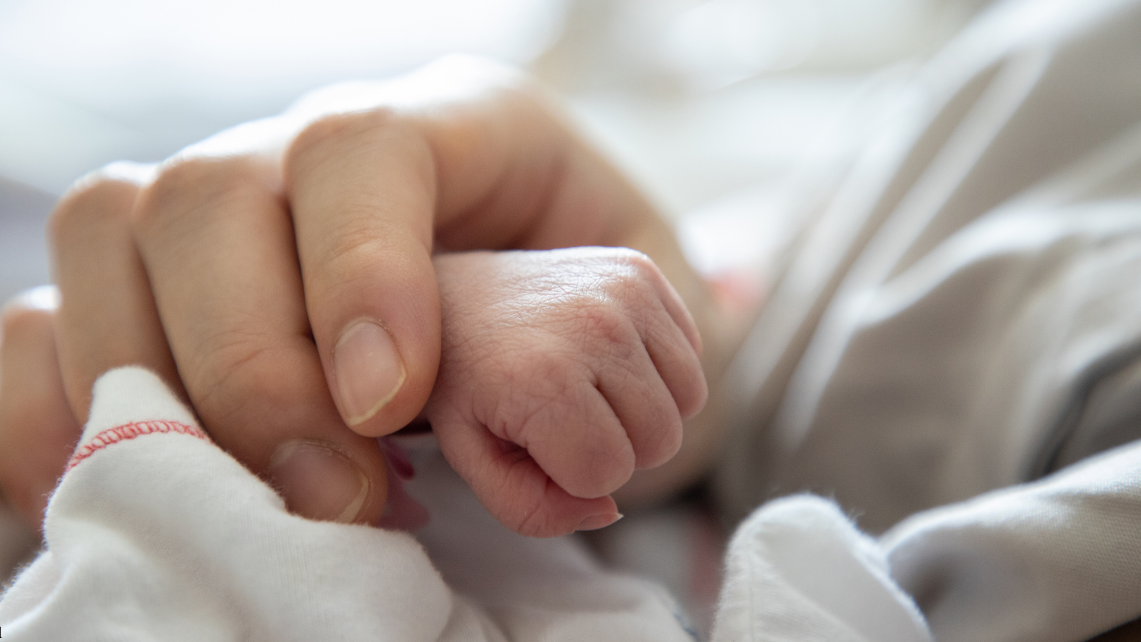 Close‑up of an adult gently holding a newborn’s tiny hand, symbolizing care and support for maternal and infant health